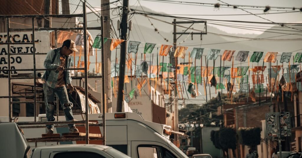Trabajador de la construcción en un andamio en una vibrante calle de la ciudad, rodeado de banderas coloridas.