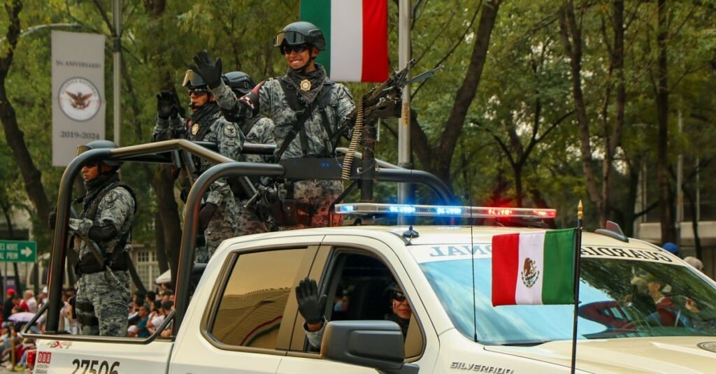 Fuerzas armadas mexicanas en un desfile con vehículos militares y banderas nacionales en la Ciudad de México.