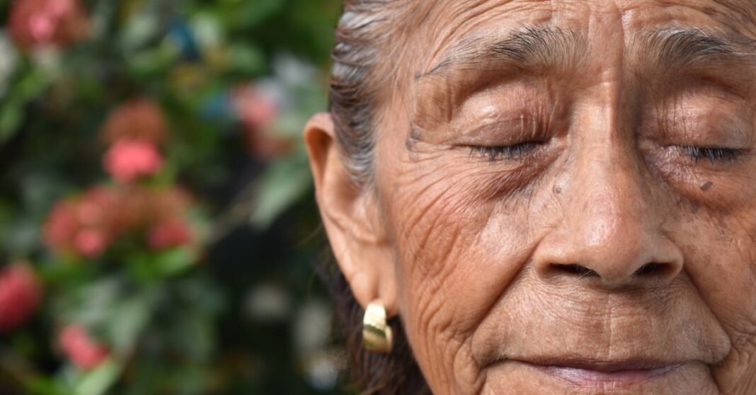 Sheinbaum pone en marcha Salud Casa por Casa para atender a adultos mayores y personas con discapacidad Primer plano de una mujer anciana con los ojos cerrados, mostrando serenidad y belleza natural en un entorno de jardín.