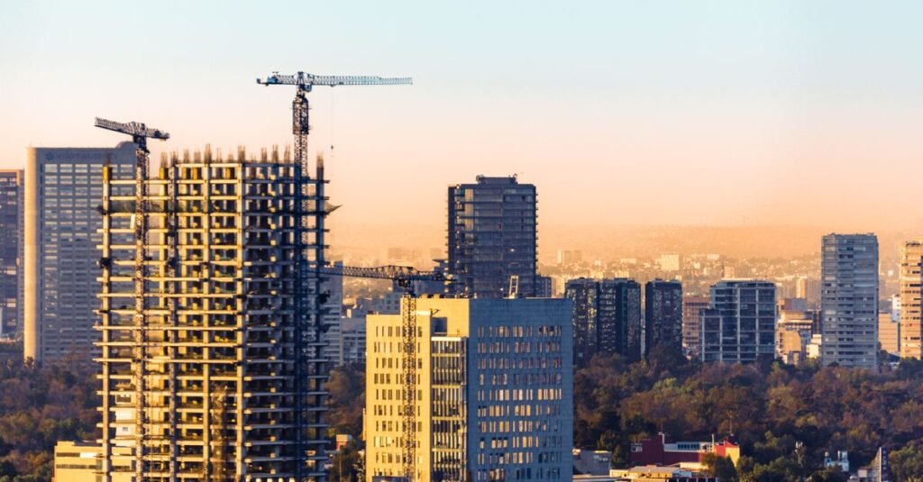 Vista aérea de grúas de construcción y rascacielos en Ciudad de México al atardecer.