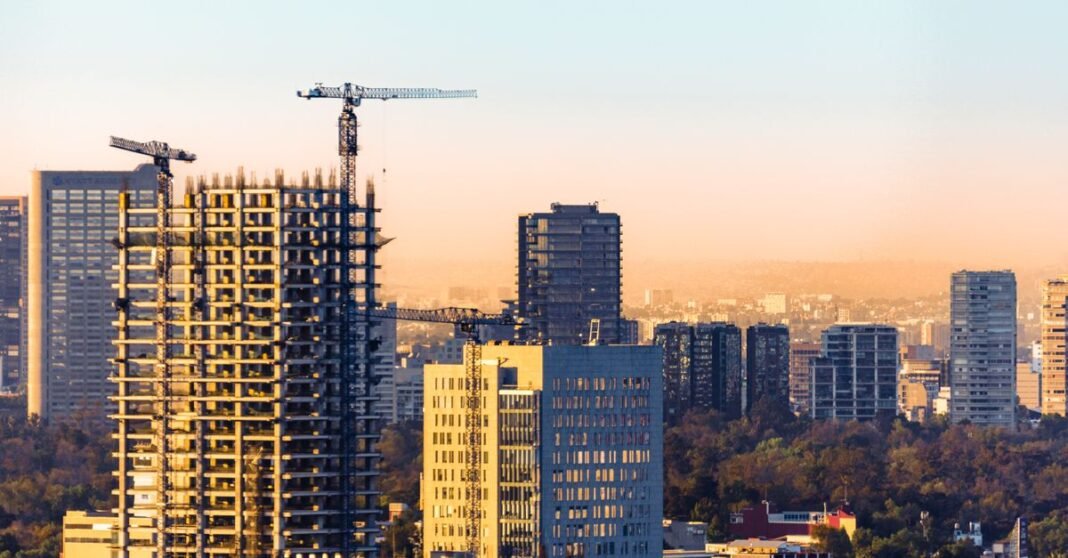 Reconstrucción por sismo alcanzaba 97% en CDMX en febrero de 2024; reportes posteriores registraron avances adicionales Vista aérea de grúas de construcción y rascacielos en Ciudad de México al atardecer.