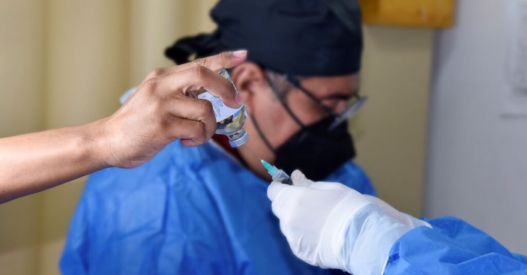 Primer plano de un trabajador de la salud llenando una jeringa desde un vial, demostrando vacunación o procedimiento médico.