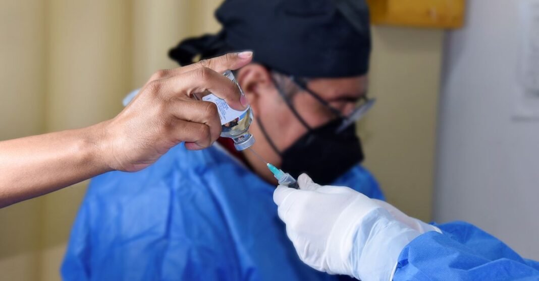 Fundación IMSS celebra 21 años como apoyo solidario del Seguro Social Primer plano de un trabajador de la salud llenando una jeringa desde un vial, demostrando vacunación o procedimiento médico.