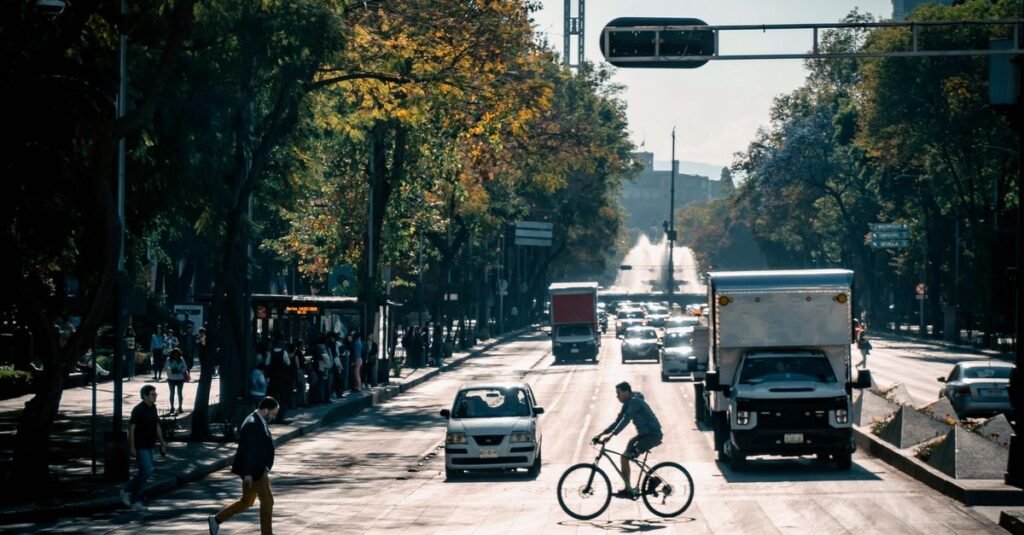 Calle concurrida en la Ciudad de México con ciclistas, peatones y tráfico bajo cielos despejados.