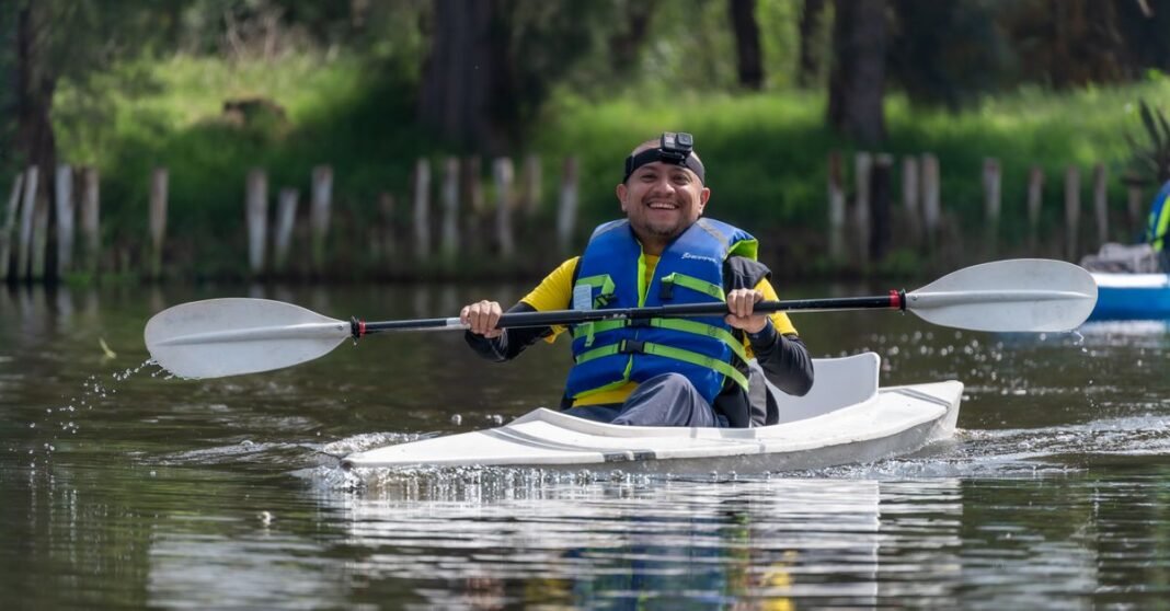 Hombre sonriendo en kayak con un remo y chaleco salvavidas en Xochimilco, México.