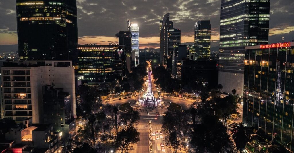 Coches y peatones en una calle urbana concurrida en Ciudad de México, bordeada de árboles y edificios.