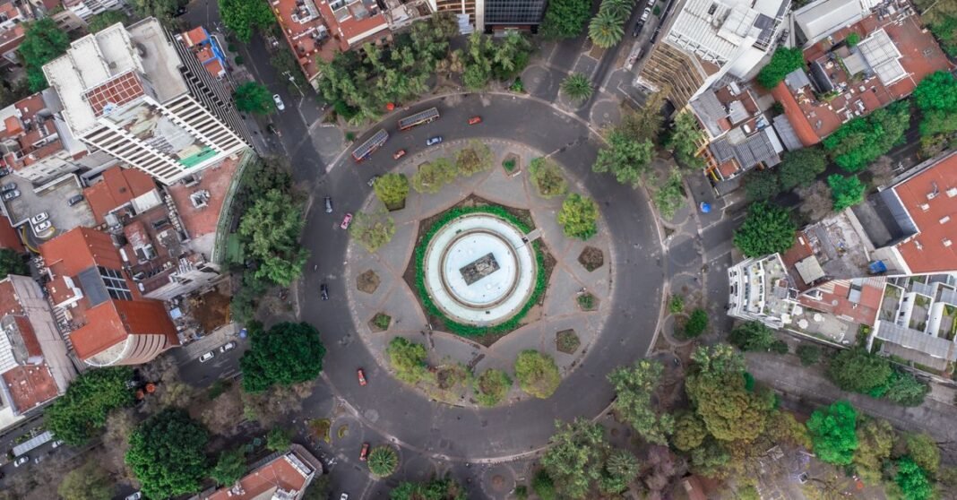 CDMX ajusta horarios de Metro y otros transportes por Nochebuena y Navidad Escena de una parada de autobús con edificios coloridos en Ciudad de México, mostrando la vida urbana local.