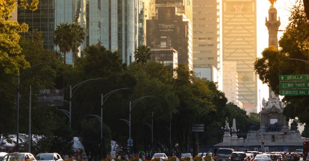 Coches y peatones en una calle urbana concurrida en Ciudad de México, bordeada de árboles y edificios.