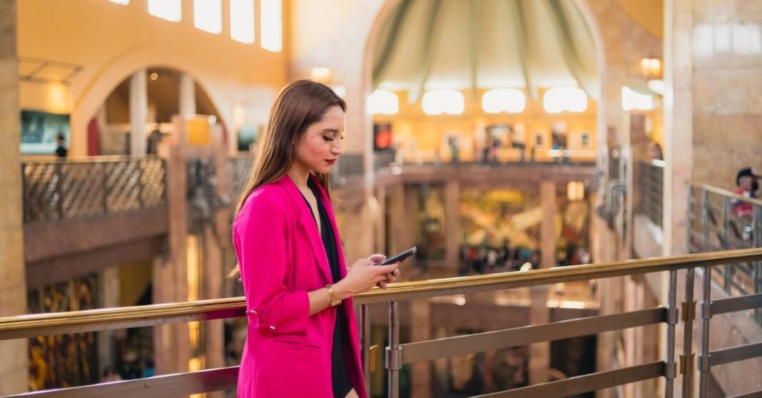 Nu México prepara su paso a banca múltiple: esto cambiará para sus clientes a partir del 6 de agosto Joven con un elegante blazer rosa usando su smartphone en un centro comercial de la Ciudad de México.