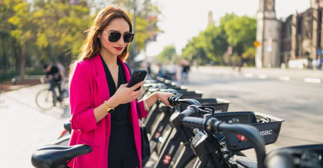 Una mujer a la moda revisa su teléfono junto a una estación de bicicletas en la Ciudad de México.