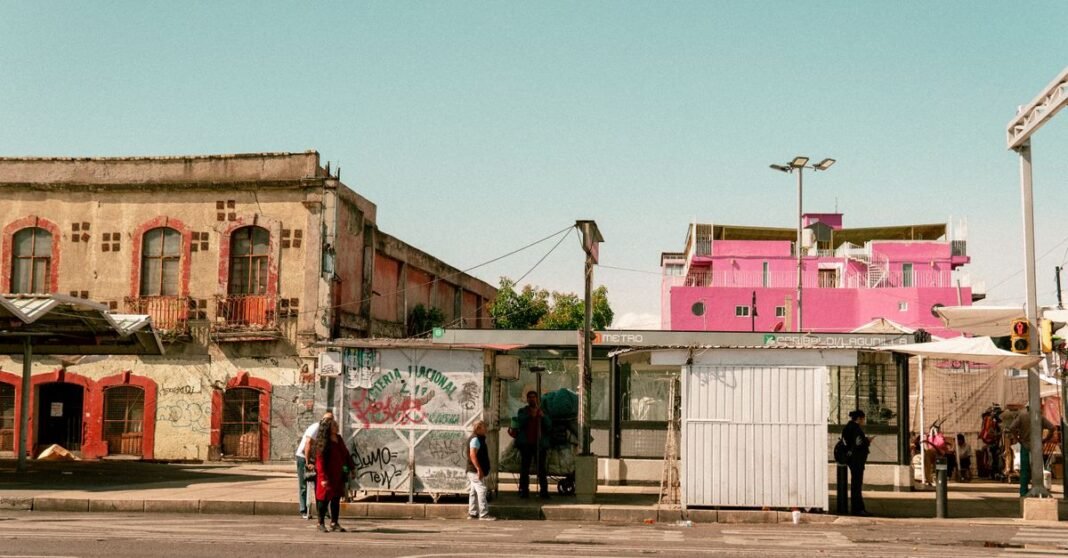 Metro de CDMX exige chalecos por línea e identificación para personal de locales comerciales Escena de una parada de autobús con edificios coloridos en Ciudad de México, mostrando la vida urbana local.