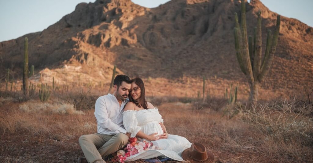 Una pareja embarazada amorosa sentada junta en un sereno paisaje desértico, abrazando la belleza de la naturaleza.