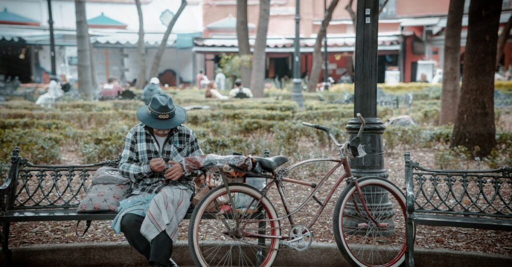 Un hombre con sombrero sentado en un banco con una bicicleta en un parque bullicioso en Ciudad de México.