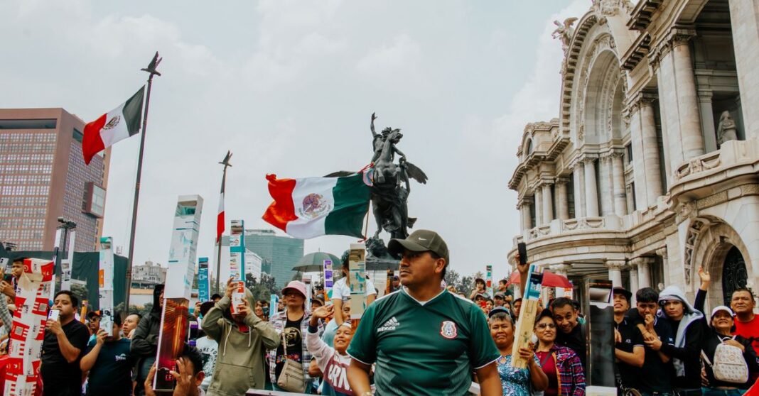 Sheinbaum suspende su participación en la mañanera por gripa, tos y fiebre Multitudes se reúnen frente al Palacio de Bellas Artes en la Ciudad de México, agitando banderas durante una celebración festiva.