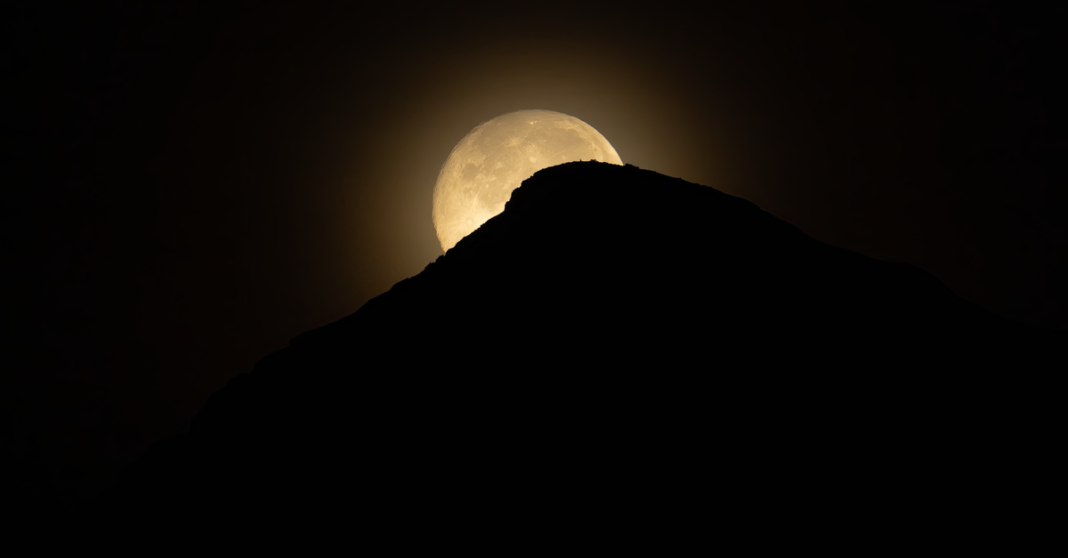 Dramática silueta de una montaña con la luna saliendo detrás, capturada en Alicante, España por la noche.