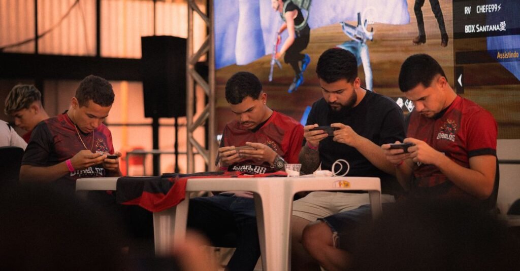 Grupo de jugadores intensamente concentrados durante un torneo de deportes electrónicos móviles en interiores.