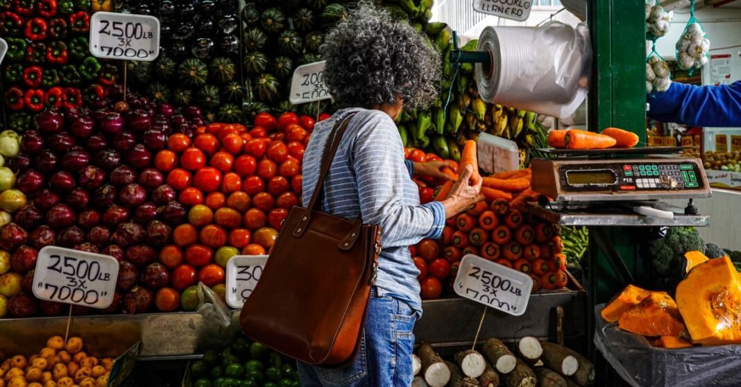Inflación en México: por qué el repunte de marzo no fue necesariamente una mala señal para Banxico Mujer comprando en un vibrante puesto de mercado local lleno de frutas y verduras frescas.
