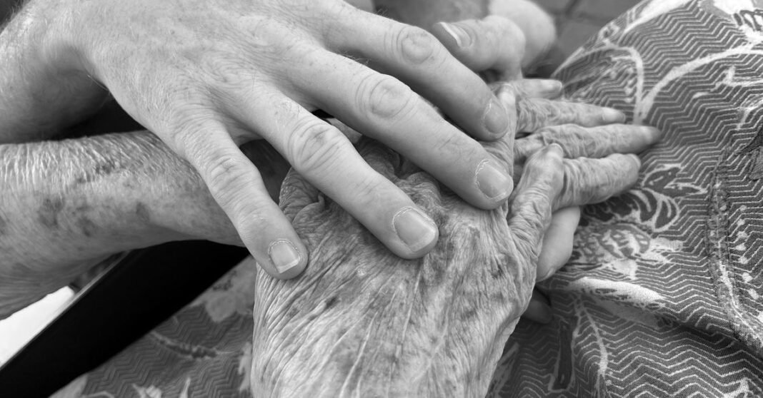 Imagen conmovedora de un adulto sosteniendo la mano de una persona mayor, simbolizando el cuidado y la conexión.
