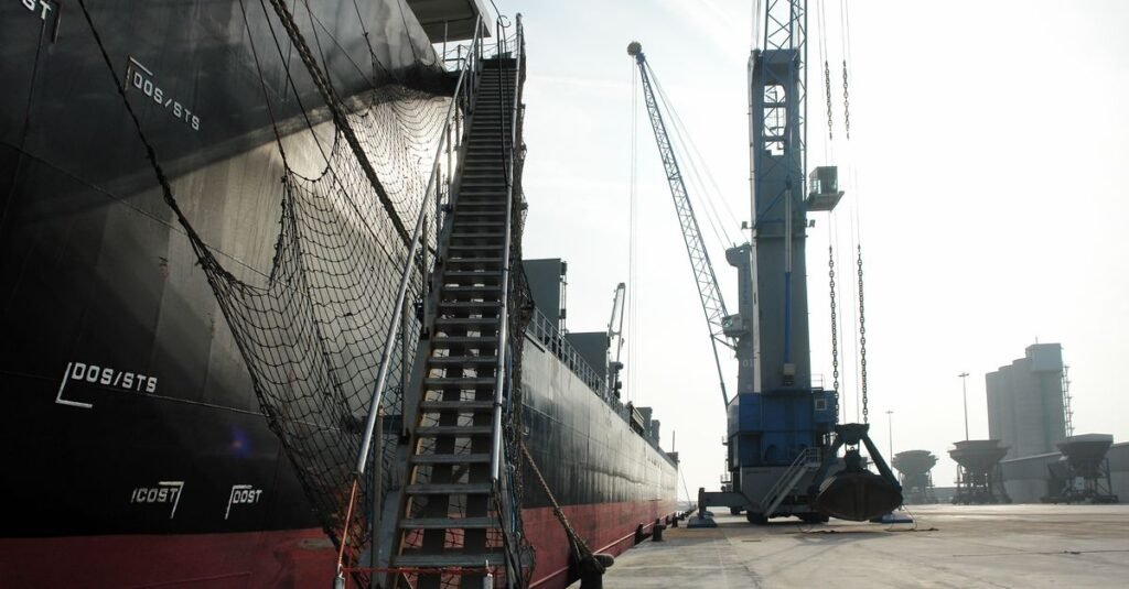 Un buque de carga atracado en un puerto industrial, con una grúa y una red de seguridad a la vista.