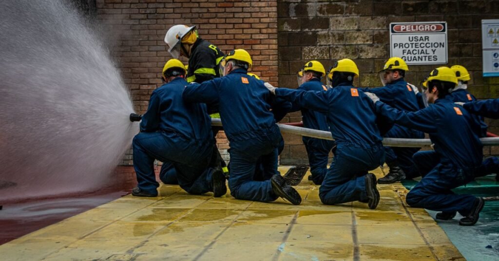 Grupo de bomberos en entrenamiento, utilizando una manguera de agua durante un simulacro, haciendo hincapié en el trabajo en equipo y la seguridad.