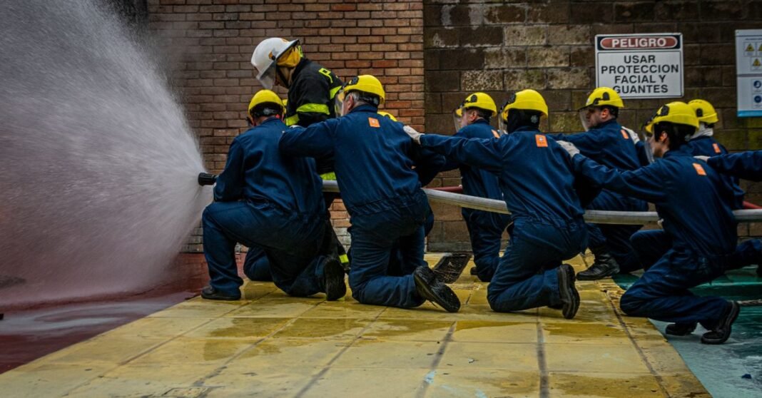 Sin confirmación independiente, reporte sobre explosión de pipa en Cuernavaca requiere verificación oficial Grupo de bomberos en entrenamiento, utilizando una manguera de agua durante un simulacro, haciendo hincapié en el trabajo en equipo y la seguridad.