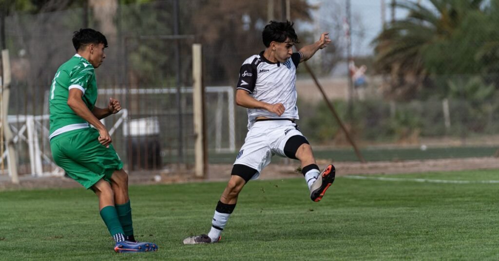 Atletas jugando al fútbol en un partido competitivo en un campo verde vibrante.