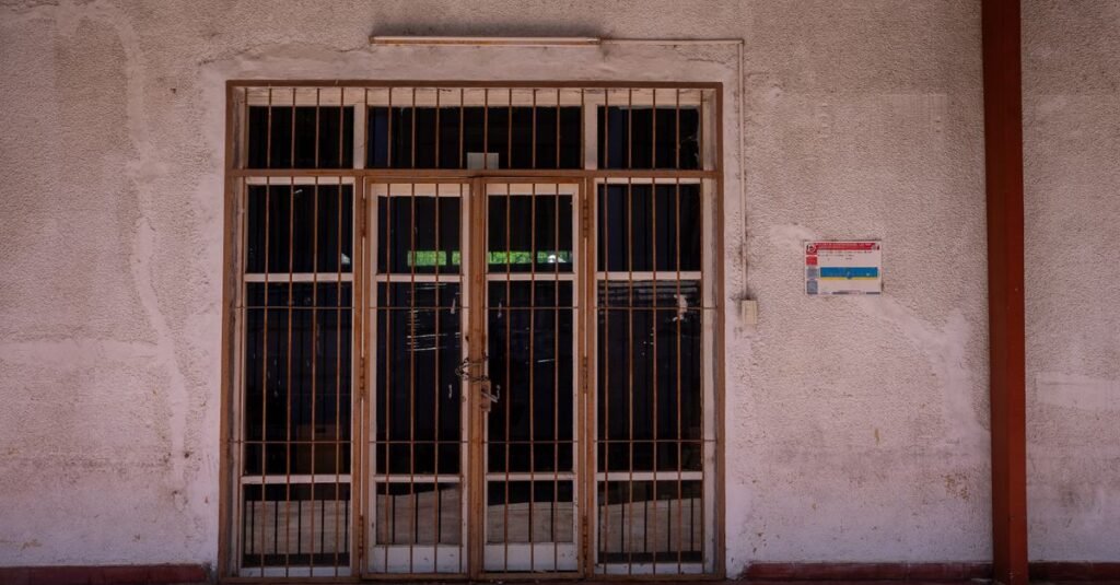 Una verja rústica de hierro en una pared texturizada con un cartel de advertencia, capturada a plena luz del día.