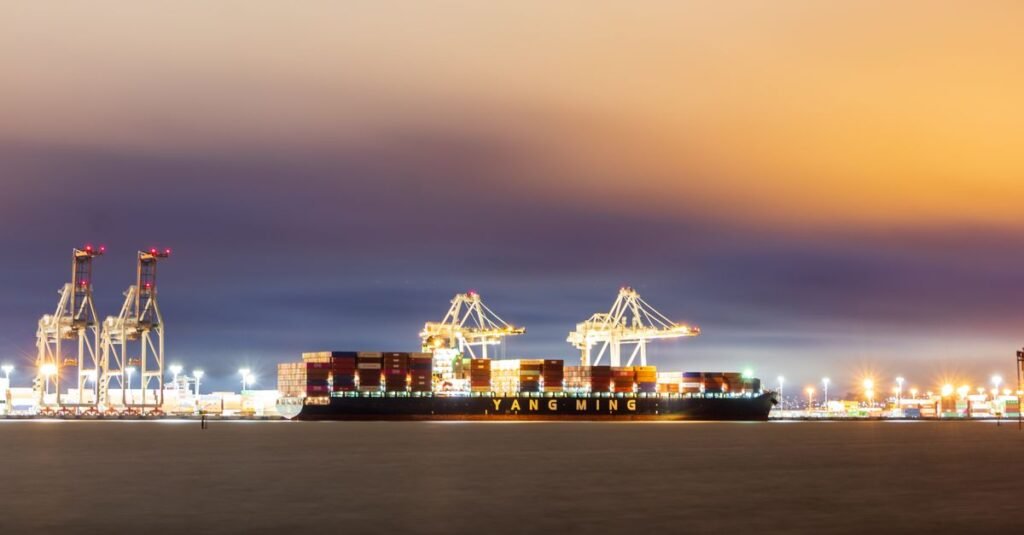Un barco de carga atracado en el puerto de Oakland al atardecer, con cielos vibrantes y grúas industriales.
