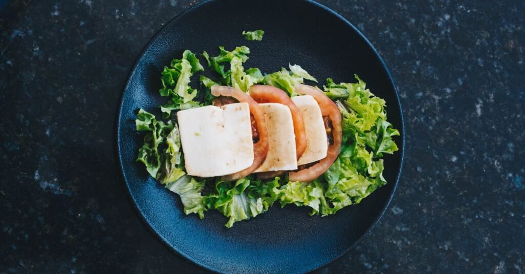 Vista superior de una ensalada fresca con queso y tomates en un plato negro, perfecta para una alimentación saludable.