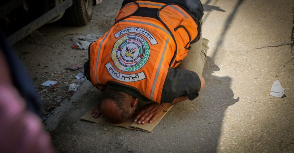 Un trabajador de emergencia con chaleco naranja reza en una calle de Gaza, representando un momento de fe en medio del caos.