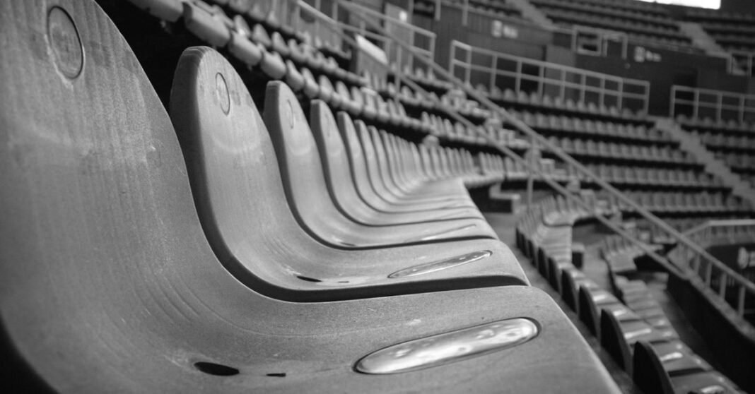 Fotografía en blanco y negro de las tribunas vacías de un estadio de Córdoba, resaltando la estructura y la atmósfera.