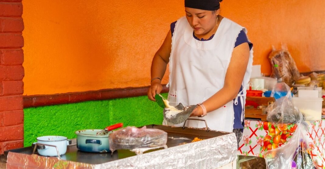 CDMX declara patrimonio cultural inmaterial los saberes del pan dulce tradicional Un vendedor ambulante en Ciudad de México exhibiendo comidas tradicionales mexicanas en una mesa colorida.